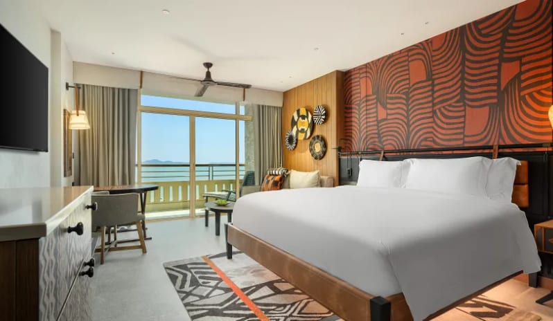 Deluxe Explorer (DBL/DBL) bed, vibrant orange tribal wall art, a geometric patterned rug, and floor-to-ceiling windows with a sea view at Centara Grand Mirage Beah Resort by Kenwood Travel
