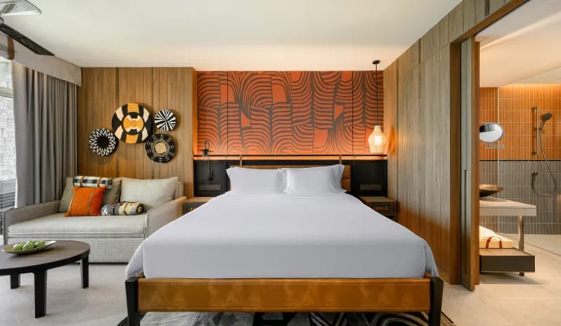 Deluxe Explorer (King) king-size bed, orange tribal-patterned headboard, wood-paneled walls with African basket art, and a view into a contemporary ensuite bathroom at Centara Grand Mirage Beah Resort by Kenwood Travel