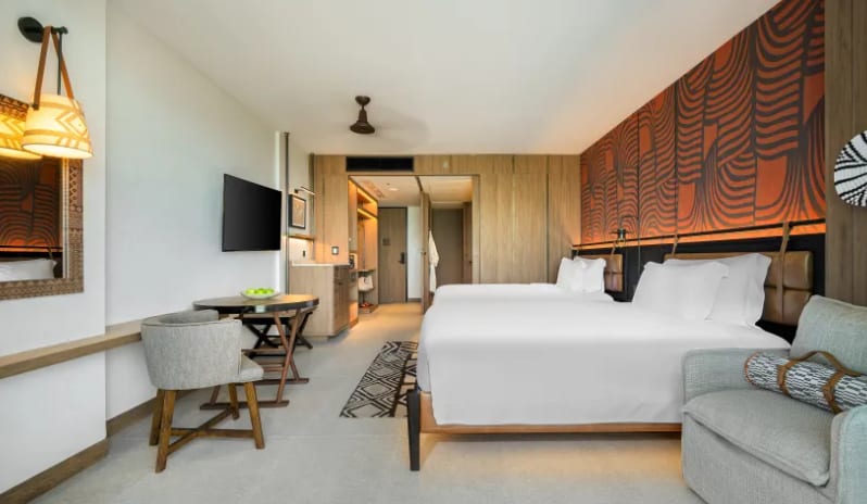 Premium Explorer (DBL/DBL) bedroom featuring white bedding, a vibrant orange patterned feature wall, wooden furnishings, and a cozy seating area with African-inspired decor at Centara Grand Mirage Beah Resort by Kenwood Travel