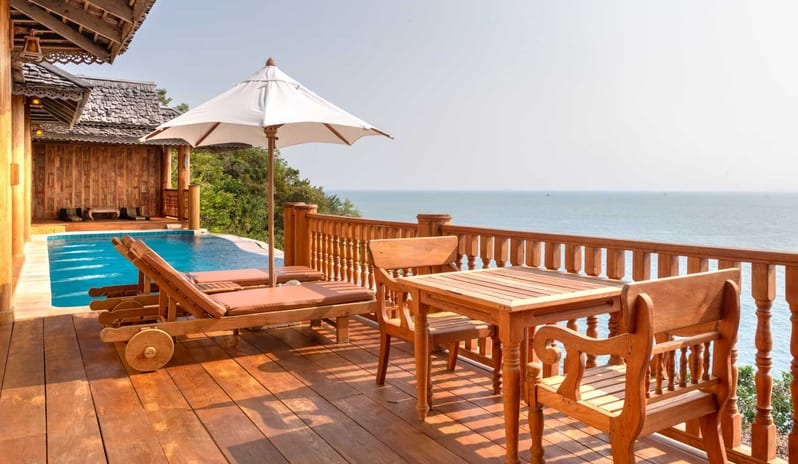 Two Bedroom Sea Water Pool Villa drenched wooden balcony of a luxury villa featuring an infinity pool, wooden lounge chairs under a white umbrella, and a dining set overlooking the calm blue ocean at Santhiya Koh Yao Yai Resort & Spa by Kenwood Travel