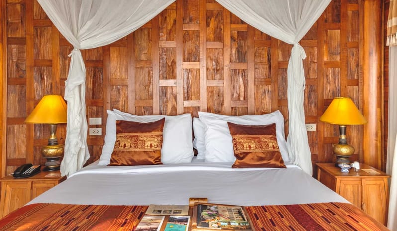 Two Bedroom Sea Water Pool Villa bedroom featuring a hand-carved teak wood paneled headboard, a white canopy bed with mosquito netting, and decorative silk elephant pillows at Santhiya Koh Yao Yai Resort & Spa by Kenwood Travel