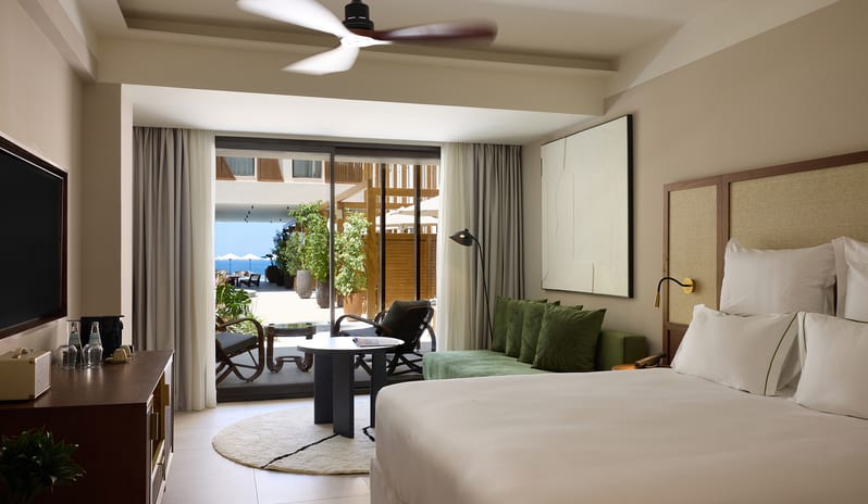 Atrium Escape Bedroom with a plush white bed, minimalist decor, and a private balcony overlooking a courtyard at Aulūs Chania, Curio Collection by Hilton by Kenwood Travel