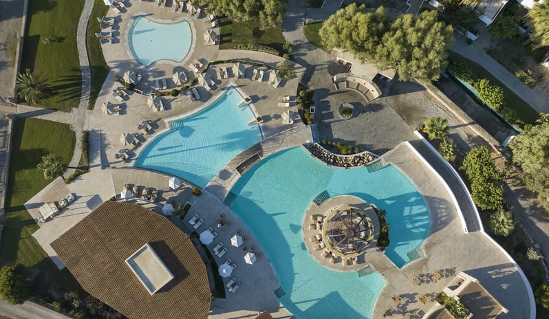 The Spiritzeria large turquoise swimming pool, a central domed gazebo bar, sun loungers, and scenic mountain views at Aulūs Lindos Rhodes, Curio Collection by Hilton by Kenwood Travel