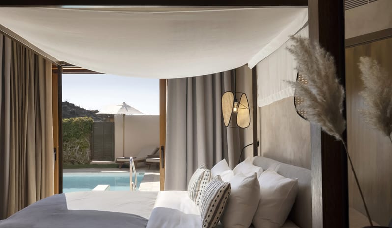 Tropical Bungalow Suite with Private Pool Bedroom Ccanopy bed with white linens, viewing a private outdoor pool and sun deck under a clear blue sky.at Aulūs Lindos Rhodes, Curio Collection by Hilton by Kenwood Travel
