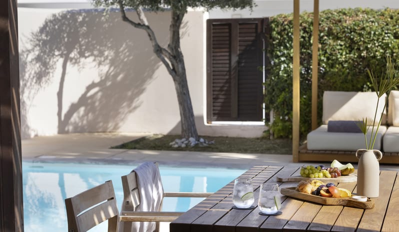 Tropical Bungalow Suite with Private Pool an outdoor wooden dining table under bright sunlight at Aulūs Lindos Rhodes, Curio Collection by Hilton by Kenwood Travel
