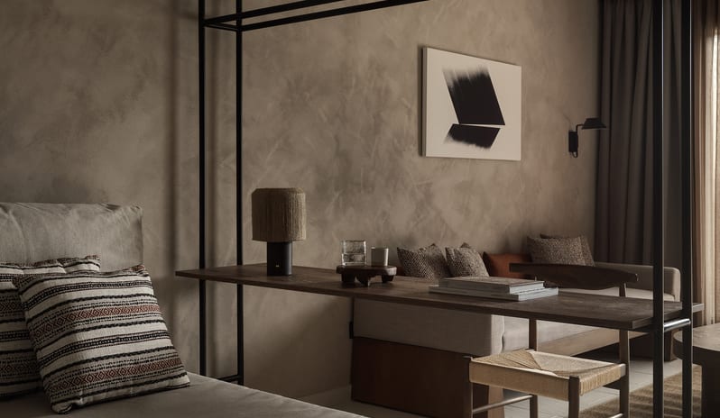 Tropical Pavilion One Bedroom Suite with Private Pool living area featuring textured plaster walls, an integrated wooden desk, and a neutral sofa with patterned accent pillows at Aulūs Lindos Rhodes, Curio Collection by Hilton by Kenwood Travel