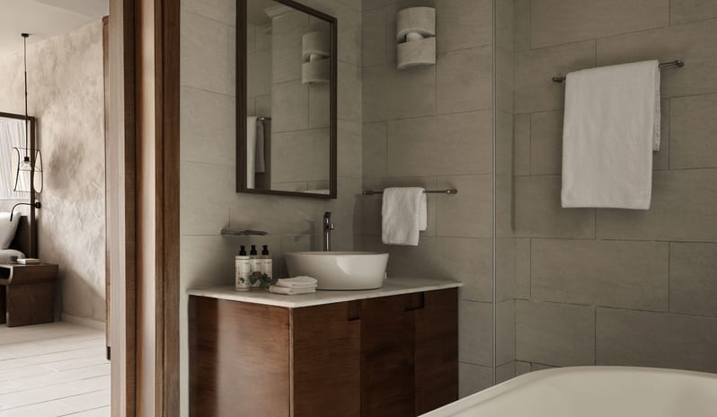 Tropical Pavilion One Bedroom Suite with Private Pool bathroom featuring a dark wood vanity with a white vessel sink, square grey tiles, and a glimpse of a white soaking tub at Aulūs Lindos Rhodes, Curio Collection by Hilton by Kenwood Travel