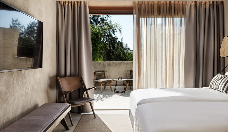 Tropical Pavilion Two Bedroom Suite with Outdoor Jacuzzi wall-mounted TV, and large sliding doors opening to a private sunny terrace with outdoor seating at Aulūs Lindos Rhodes, Curio Collection by Hilton by Kenwood Travel