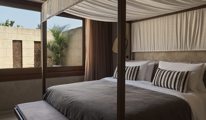 Tropical Pavilion Two Bedroom Suite with Outdoor Jacuzzi canopy bed, neutral Earth tones, and a view of a private outdoor terrace with a palm tree at Aulūs Lindos Rhodes, Curio Collection by Hilton by Kenwood Travel