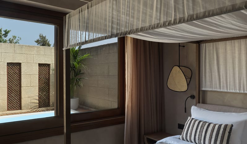 Tropical Pavilion Two Bedroom Suite with Outdoor Jacuzzi canopy bed, neutral Earth tones, and a view of a private outdoor terrace with a palm tree at Aulūs Lindos Rhodes, Curio Collection by Hilton by Kenwood Travel