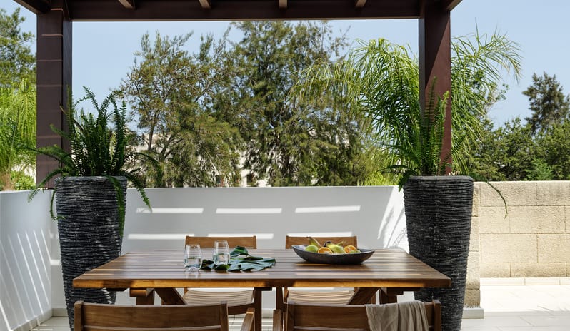 Tropical Pavilion Two Bedroom Suite with Outdoor Jacuzzi Modern wooden outdoor dining set under a pergola at the  view of lush greenery at Aulūs Lindos Rhodes, Curio Collection by Hilton by Kenwood Travel