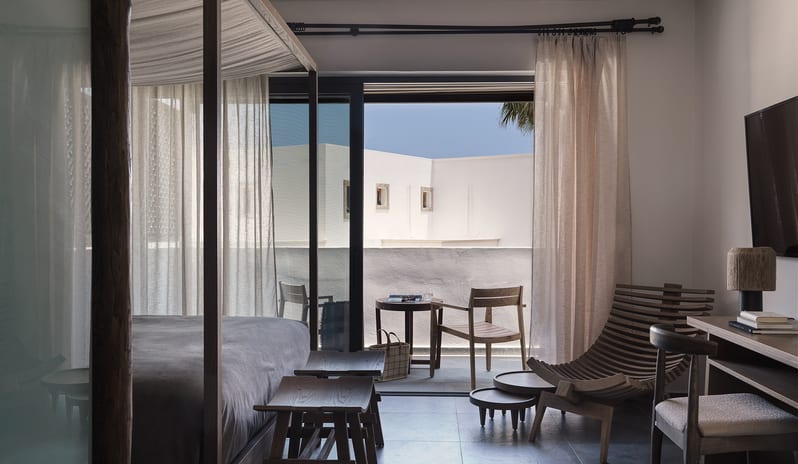 Tropical Zen Bungalow Suite Bedroom Bedroom bedroom with natural wood finishes, canopy bed, and floor-to-ceiling windows showing a sunny balcony at Aulūs Lindos Rhodes, Curio Collection by Hilton by Kenwood Travel