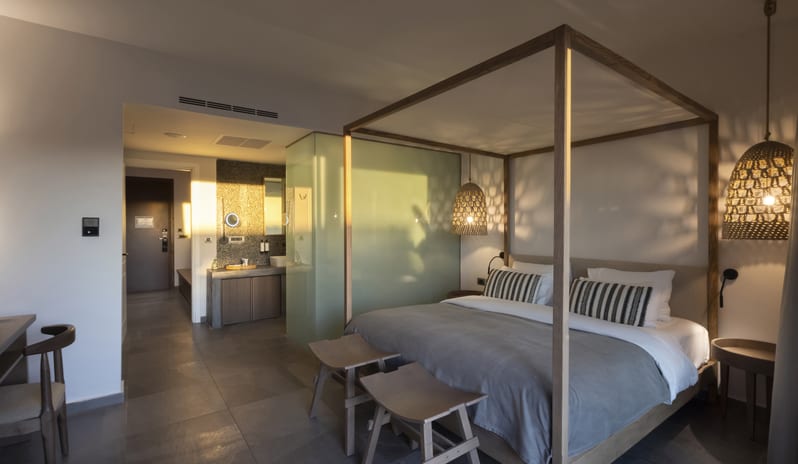 Tropical Zen Bungalow Suite Bedroom With a Canopy Bed, Stylish Rattan Lamps, and Stone Tile Flooring at Aulūs Lindos Rhodes, Curio Collection by Hilton by Kenwood Travel