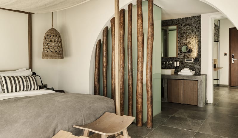 Tropical Zen Bungalow Suite with Private Pool canopy bed, woven pendant light, and a unique arched bathroom entrance with vertical log room dividers and pebble tile walls at Aulūs Lindos Rhodes, Curio Collection by Hilton by Kenwood Travel