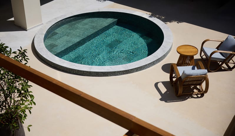 Atrium Escape circular plunge pool with turquoise water, surrounded by tan stone tile and rattan patio furniture at Aulūs Chania, Curio Collection by Hilton by Kenwood Travel