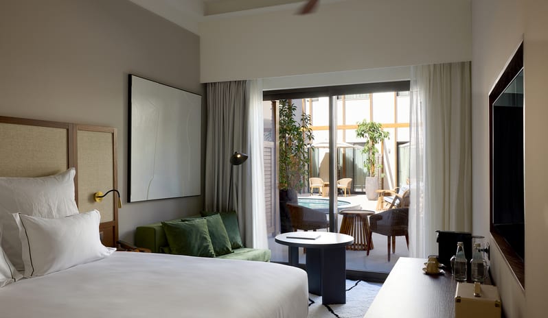 Atrium Escape Bedroom with a plush white bed, minimalist decor, and a private balcony overlooking a courtyard at Aulūs Chania, Curio Collection by Hilton by Kenwood Travel