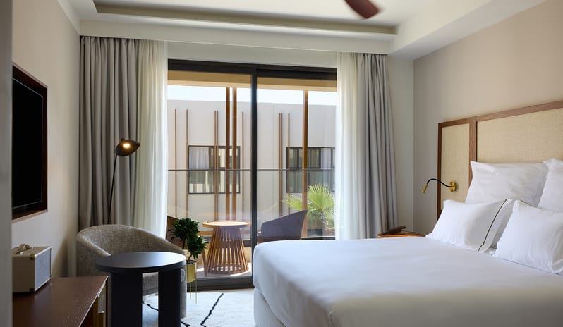 Atrium Escape Bedroom with a plush white bed, minimalist decor, and a private balcony overlooking a courtyard at Aulūs Chania, Curio Collection by Hilton by Kenwood Travel