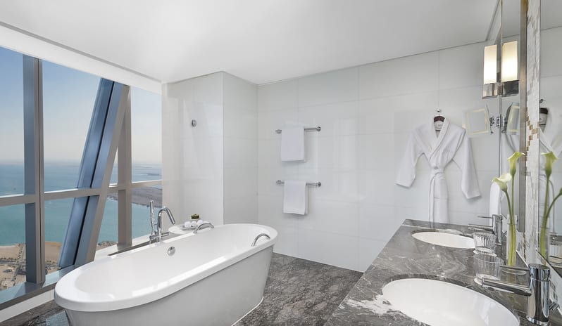 Etihad Suite bathroom with sea view, freestanding bathtub, double marble vanity, bathrobe, and floor-to-ceiling windows overlooking the ocean at Conrad Abu Dhabi Etihad Towers by Kenwood Travel