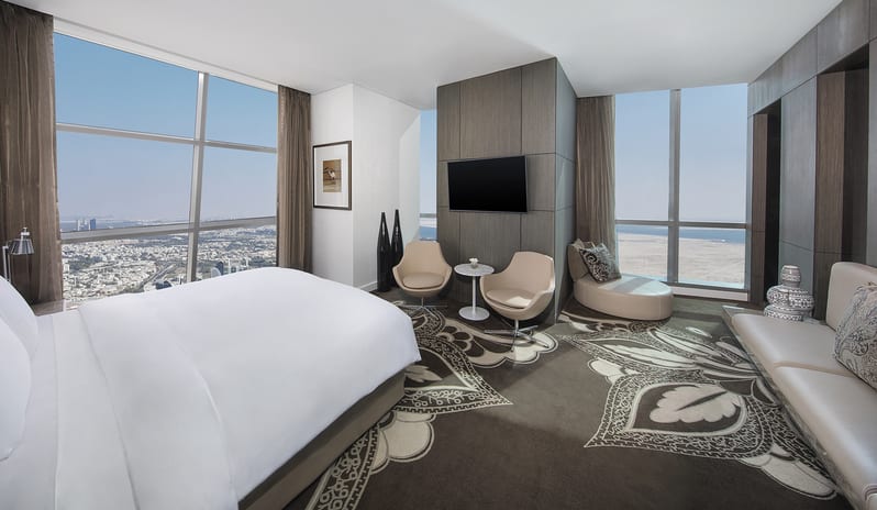 Etihad Suite bedroom with sea view, king-size bed, modern seating area, and floor-to-ceiling windows overlooking the coastline at Conrad Abu Dhabi Etihad Towers by Kenwood Travel
