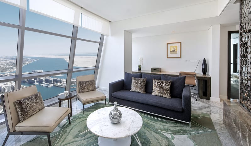 Etihad Suite bedroom living room with sea view, modern sofa seating, marble coffee table, work desk, and floor-to-ceiling windows overlooking the coastline at Conrad Abu Dhabi Etihad Towers by Kenwood Travel