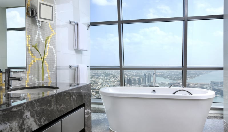 Premier Family Room with Sea View bathroom with freestanding bathtub, marble vanity, and floor-to-ceiling windows offering a panoramic sea and city view at Conrad Abu Dhabi Etihad Towers by Kenwood Travel