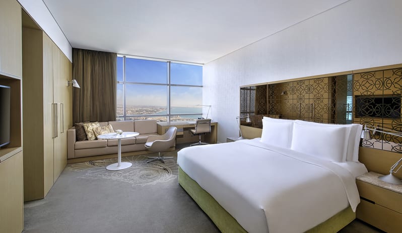 Premier Family Room with Sea View bedroom featuring a king bed, lounge area, and large window with a scenic ocean view at Conrad Abu Dhabi Etihad Towers by Kenwood Travel