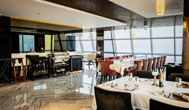 Ray's Grill Restaurant with elegant table settings, marble floors, open service station, and floor-to-ceiling windows offering a panoramic city view at Conrad Abu Dhabi Etihad Towers by Kenwood Travel
