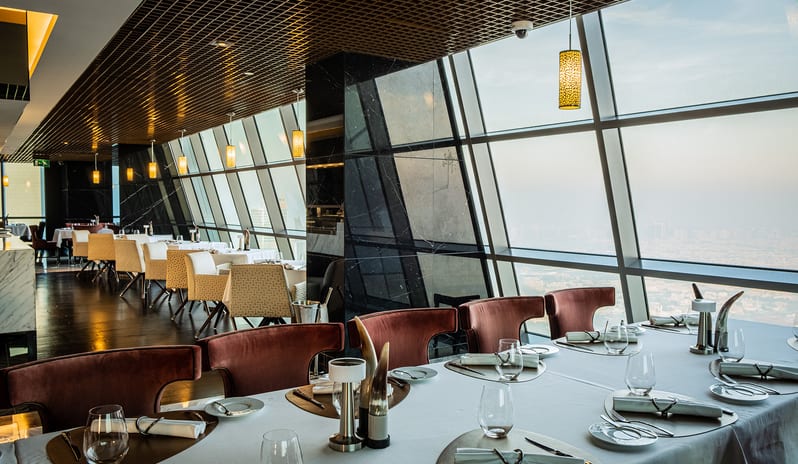 Ray's Grill Restaurant with elegant table settings, marble floors, open service station, and floor-to-ceiling windows offering a panoramic city view at Conrad Abu Dhabi Etihad Towers by Kenwood Travel