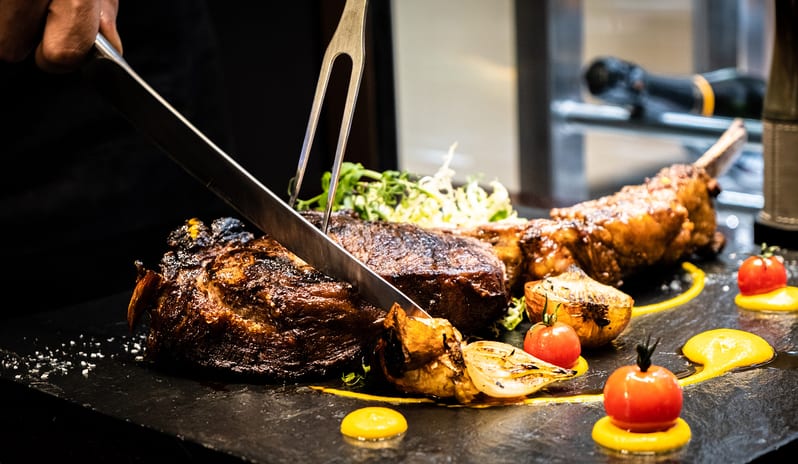 Ray's Grill Chef slicing a grilled tomahawk steak with roasted vegetables at Conrad Abu Dhabi Etihad Towers by Kenwood Travel