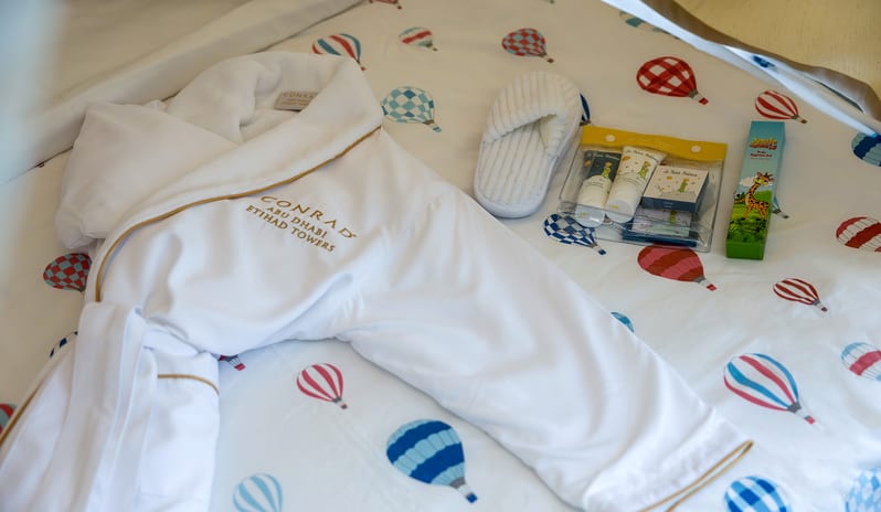 Premier Family Room with Sea View bathroom kids welcome amenities including a soft bathrobe, children’s toiletries, slippers, and playful balloon-print bedding at Conrad Abu Dhabi Etihad Towers by Kenwood Travel