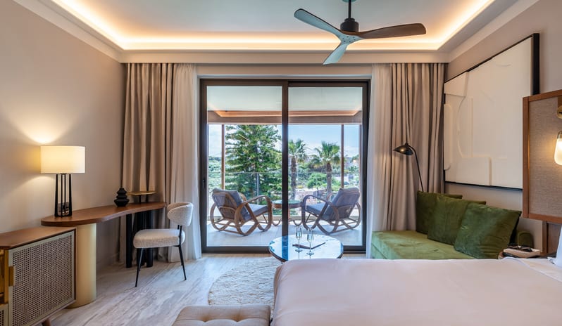 Tropical Escape private balcony with wicker lounge chairs and a tropical view at Aulūs Chania, Curio Collection by Hilton by Kenwood Travel
