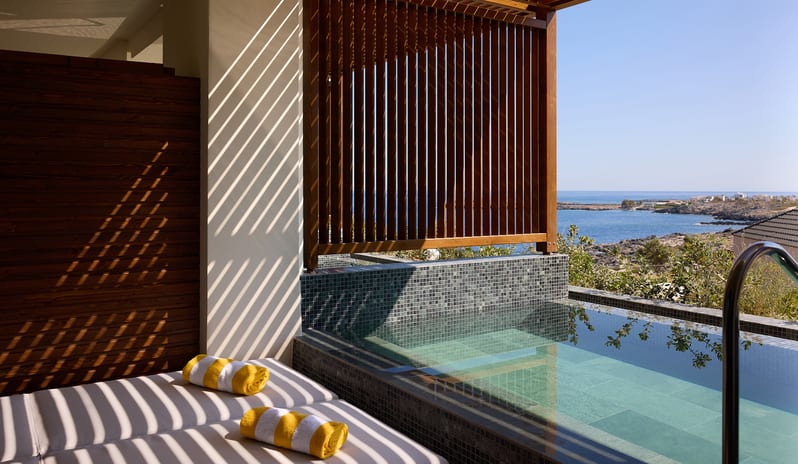 Horizon Open Plan Suite with Plunge Pool two white sun loungers with yellow striped towels, and a wooden pergola, overlooking a mountain landscape with palm trees at Aulūs Chania, Curio Collection by Hilton by Kenwood Travel