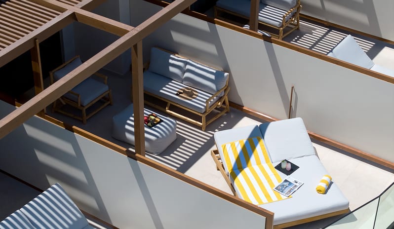 Horizon Open Plan Suite with Plunge Pool featuring bamboo outdoor sofas, large sunbeds with yellow towels, and a wooden beam pergola casting shadows at Aulūs Chania, Curio Collection by Hilton by Kenwood Travel