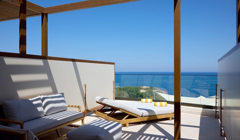 Infinite Sea View Escape Bedroom Private terrace under a wooden pergola, featuring a comfortable outdoor sofa and a double daybed with yellow striped towels at Aulūs Chania, Curio Collection by Hilton by Kenwood Travel
