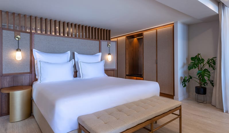 Sea View Grande Suite with Private Pool Bedroom with a tufted bench, warm pendant lighting, and a monstera plant at Aulūs Chania, Curio Collection by Hilton by Kenwood Travel
