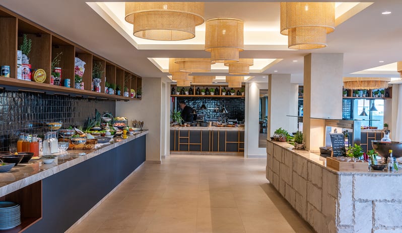 The Island Buffet Restaurant Interior view modern coastal design, rattan pendant lighting at Aulūs Chania, Curio Collection by Hilton by Kenwood Travel