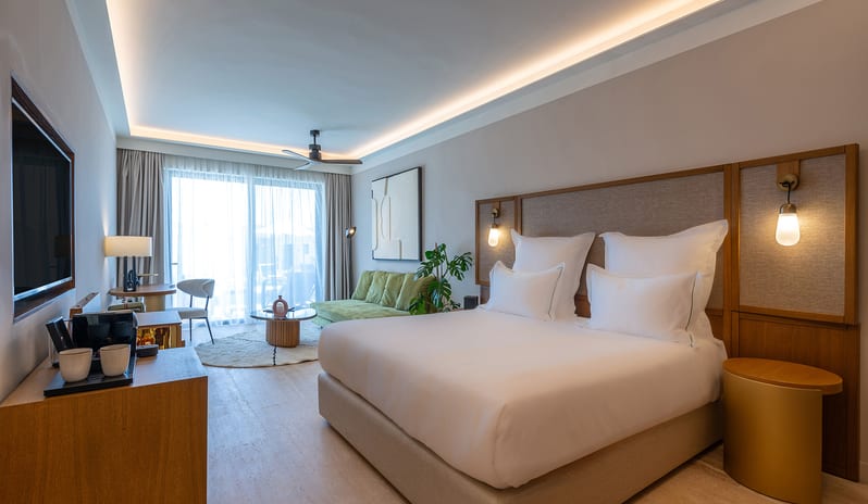 Tropical Open Plan Suite (with shared pool) Bedroom with white linens, a curved wood-paneled wall, green velvet seating, and marble accents at Aulūs Chania, Curio Collection by Hilton by Kenwood Travel