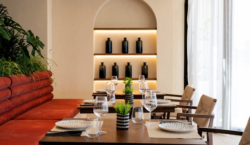 Yellow Sea Restaurant idining area featuring a burnt-orange terracotta ribbed booth, dark wood tables set with patterned plates and wine glasses at Aulūs Chania, Curio Collection by Hilton by Kenwood Travel