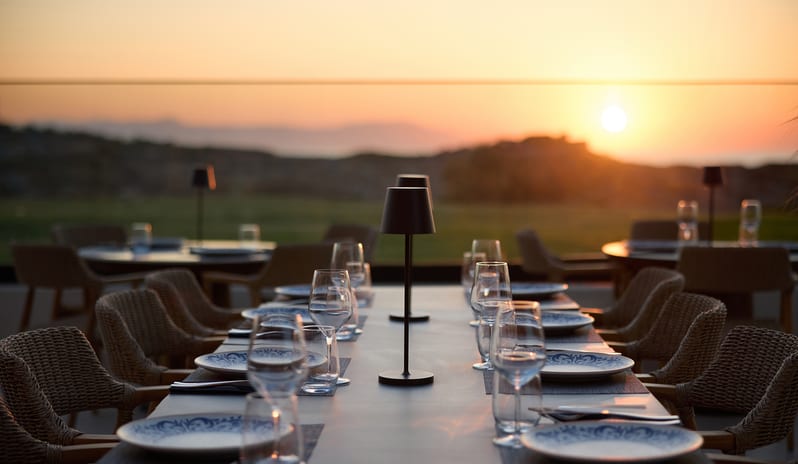 Yellow Sea Restaurant dining area featuring a burnt-orange terracotta ribbed booth, dark wood tables set with patterned plates and wine glasses at Aulūs Chania, Curio Collection by Hilton by Kenwood Travel