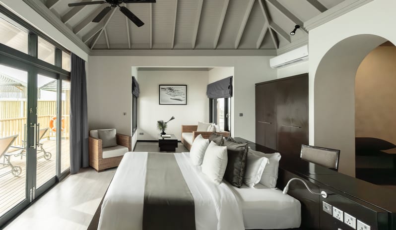 Bedroom featuring a high vaulted ceiling, king-size bed with white linens, and large glass doors opening to a private wooden deck at Al Waha resort at Sun Siyam Iru Fushi-Sunset Horizon Water Villa with Pool  by Kenwood Travel