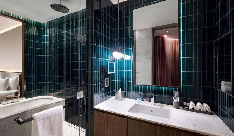 Bathroom showcasing deep emerald green vertical tiling, a marble-encased soaking tub, a walk-in rainfall shower, and a white marble vanity with a large backlit mirror at W Dubai - Mina Seyahi by Kenwood Travel