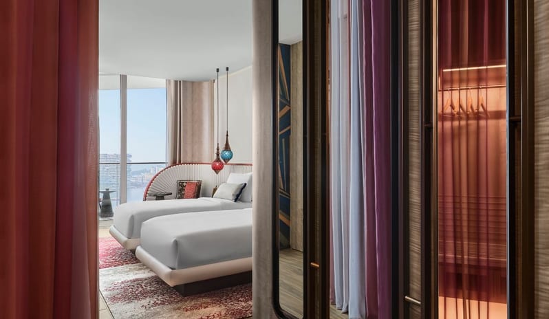 Family Corner Bedroom featuring white fluted headboards, colorful Arabic-inspired pendant lights, a private balcony with sea views, and bold geometric wall art at W Dubai - Mina Seyahi by Kenwood Travel