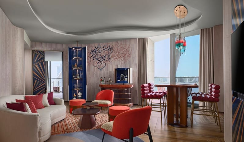 Family Suite  Living room Curved cream sofa, vibrant red lounge chairs, Arabic calligraphy wall art, and a designer bar area with floor-to-ceiling balcony viewsat W Dubai - Mina Seyahi by Kenwood Travel