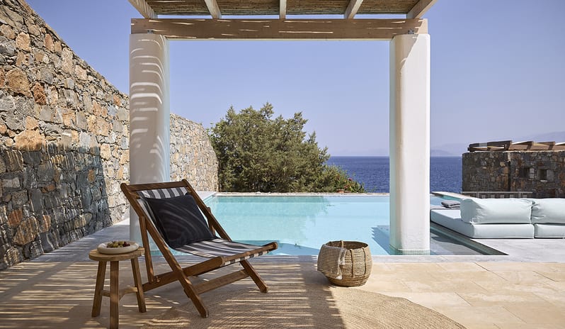 Three Bedroom Thalassa Villa Private Pool Seafront wooden lounge chair under a rustic pergola, a woven rug, and panoramic views of the Mediterranean Sea at St.Nicolas Bay Resort by Kenwood Travel