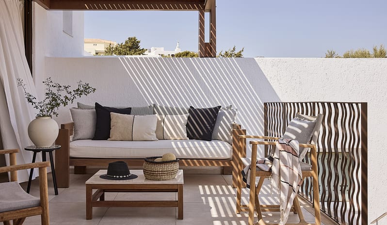 Three Bedroom Thalassa Villa Private Pool Seafront wooden outdoor sofa with plush cushions, a marble-top coffee table, and stylish pergola shadows against a white wall at St.Nicolas Bay Resort by Kenwood Travel