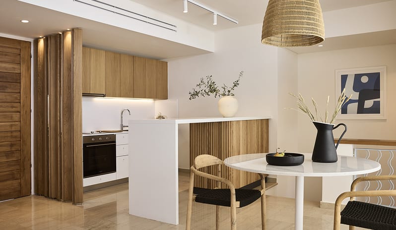 Three Bedroom Thalassa Villa Private Pool Seafront light wood cabinetry, a white breakfast bar, a marble dining table with woven chairs, and a large wicker pendant light at St.Nicolas Bay Resort by Kenwood Travel