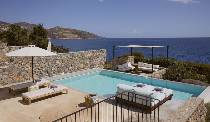 Three Bedroom Thalassa Villa Private Pool Seafront sun loungers with umbrellas, a shaded outdoor lounge area, and panoramic seafront views of the Mediterranean coastline at St.Nicolas Bay Resort by Kenwood Travel