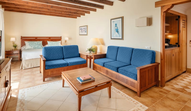 Double Superior Seaview blue upholstered wooden sofas, a rustic coffee table, terracotta tiled floors with decorative inlays, and a bedroom area with exposed timber ceiling beams at Princesa Yaiza Suite Hotel Resort by Kenwood Travel