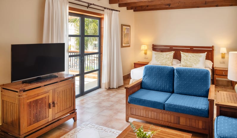 Double Superior Relax hotel room with wood beam ceilings, large flat-screen TV on a wooden console, and a comfortable blue lounge chair at Princesa Yaiza Suite Hotel Resort by Kenwood Travel