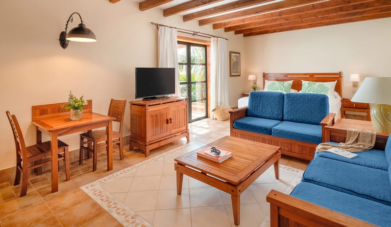 Double Superior rustic wooden ceiling beams, two blue sofas, a coffee table, and a large bed in a Mediterranean-style interior at Princesa Yaiza Suite Hotel Resort by Kenwood Travel